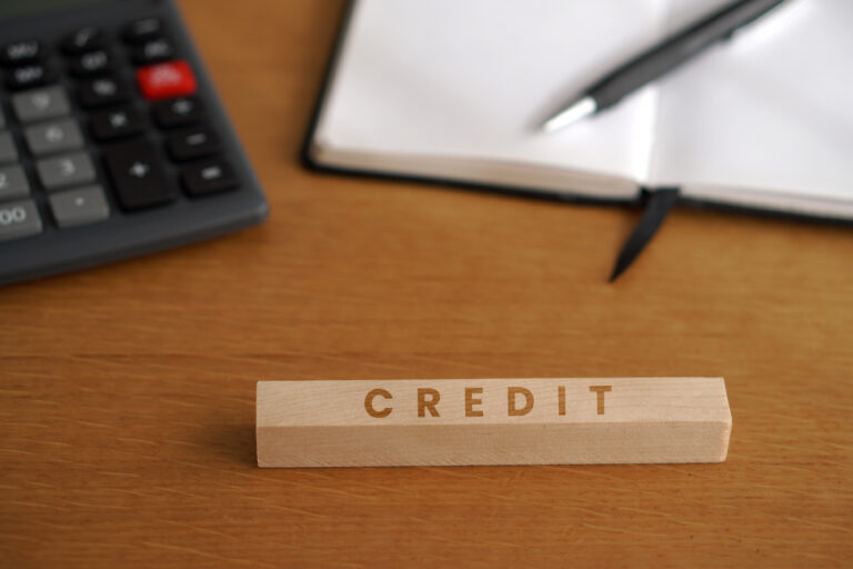 Conceito de o que é originação de crédito, ilustrado por um bloco com a palavra "Credit", calculadora, caderno e caneta em uma mesa de trabalho.
