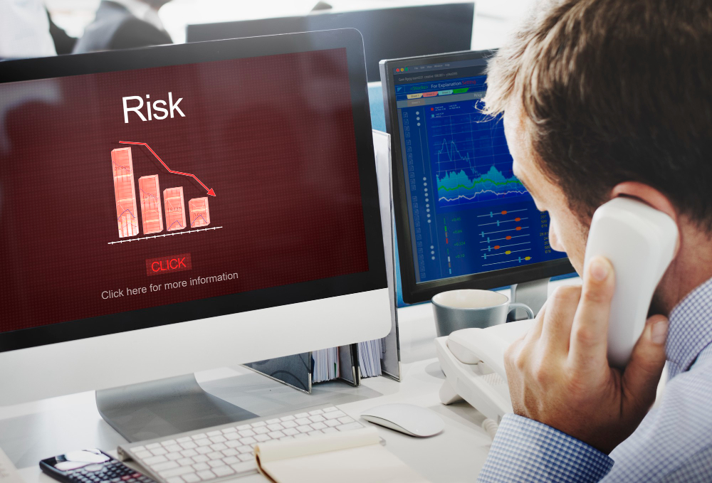 Gestão de risco representada por profissional analisando gráficos financeiros e indicador de queda em monitores de computador.